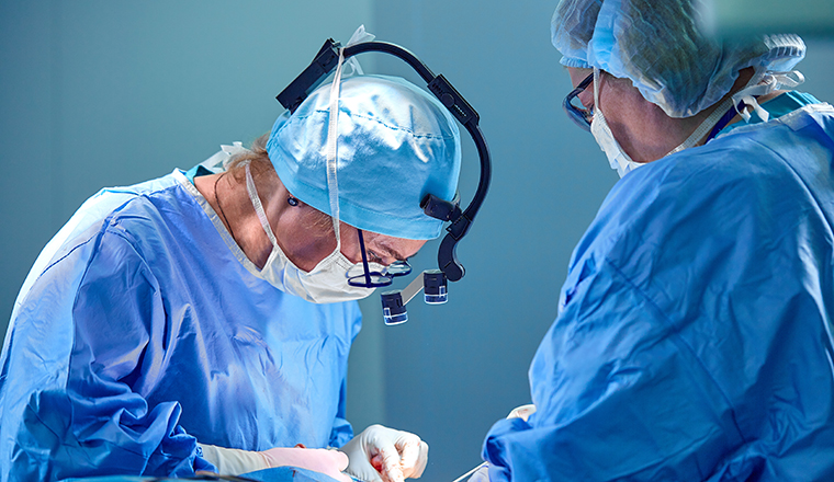 Surgeon and his assistant performing cosmetic surgery in hospital operating room. Surgeon in mask wearing loupes during medical procadure. Breast augmentation, enlargement, enhancement