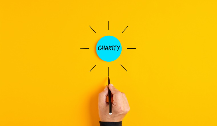 The word charity written on a blue circle badge with male hand drawing rays around it.