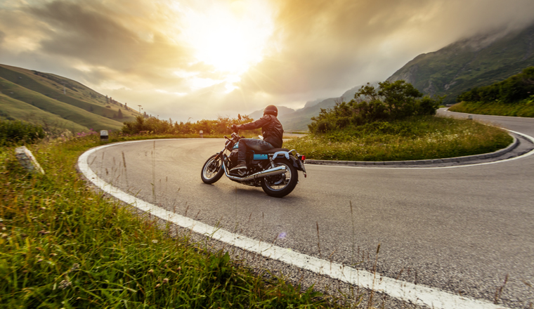 Motorcycle driver riding in Alpine landscape. Lifestyle photo with motion blur effect.