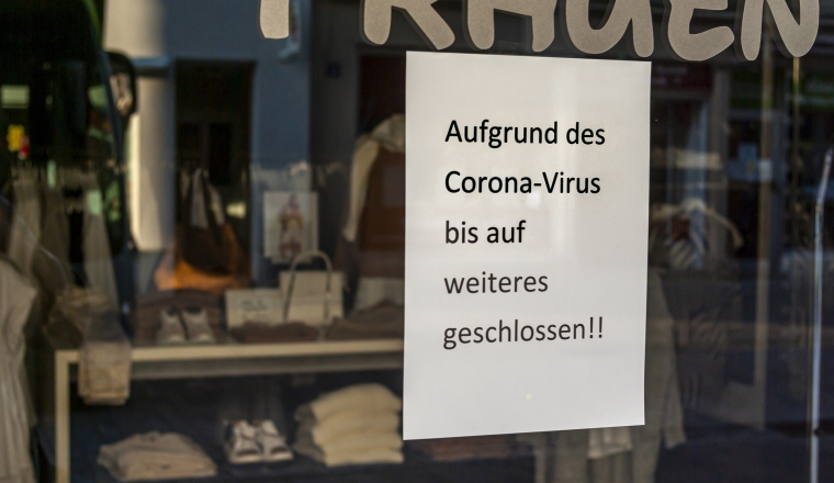 Shop window of a shop with a sign "Closed because of the Corona virus", in German, with displays and the reflection of the surroundings in blur at the time of the Corona Covid-19 pandemic in March 2020