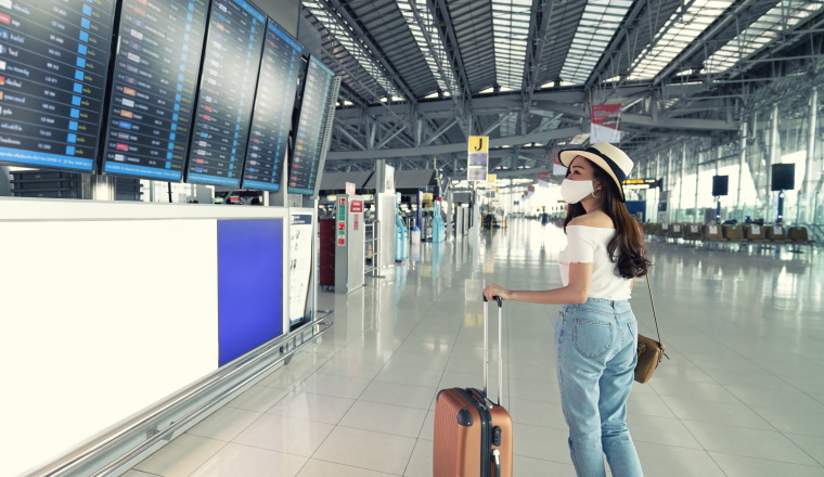 Banner photo of Asian female wearing face mask with suitcase checking flight cancellation status on airport information board in empty airport. airline bankrupt, airline crisis or new normal concept
