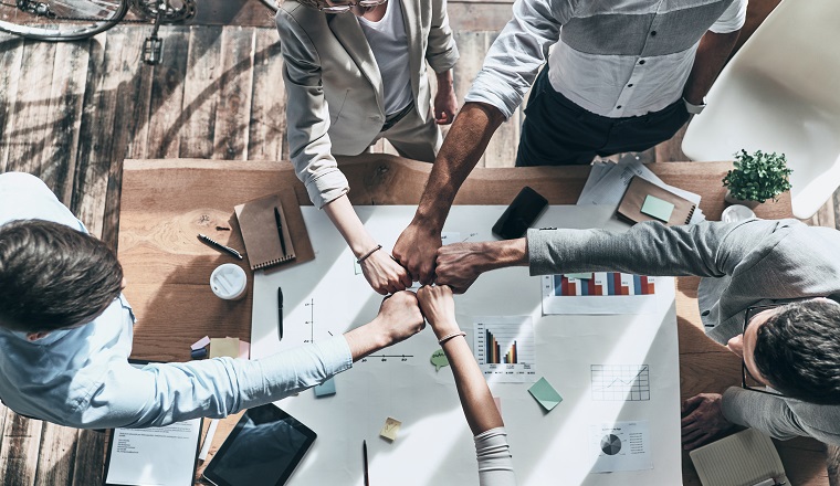 Cooperation. Close up top view of business colleagues holding fists together in a symbol of unity while working in the creative office