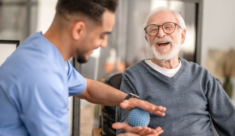 Joyous aged man undergoing a session of physical therapy conducted by an experienced rehabilitation doctor