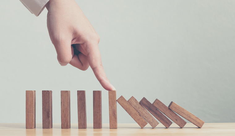 Hand stopping wooden domino business crisis effect or risk protection concept