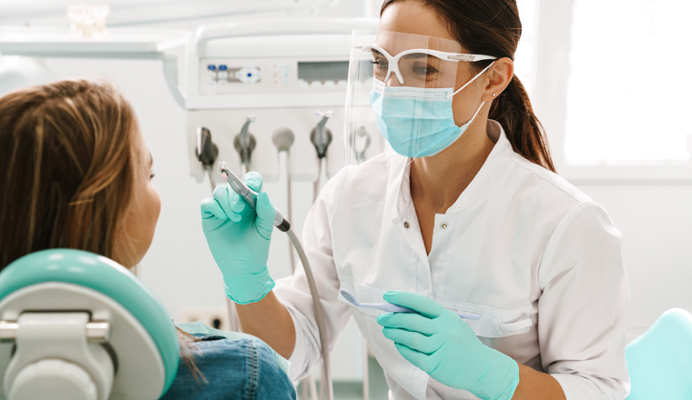 European mid pleased dentist woman in face mask working in dental clinic