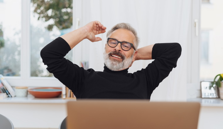 Satisfied businessman stretching his arms and smiling with closed eyes as he relaxes back in his chair at the office