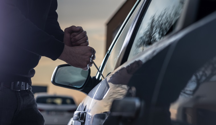 Auto thief in black balaclava trying to break into car with screwdriver. Car thief, car theft