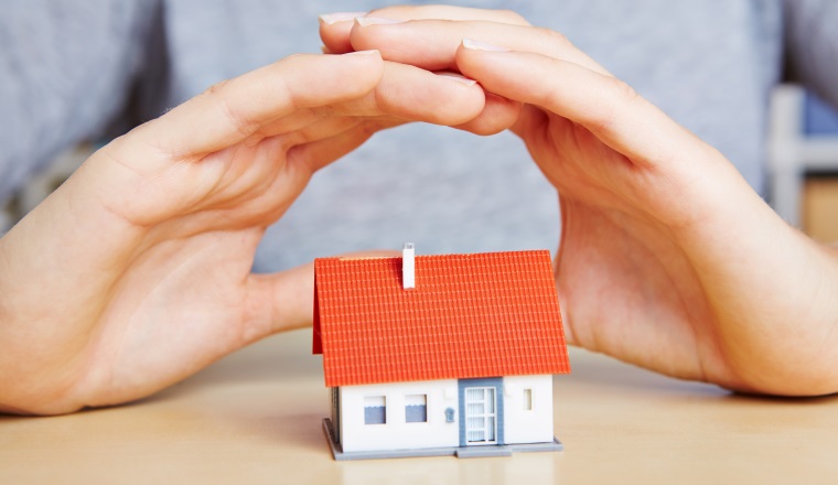 Zwei Hände schützen ein kleines Haus wie eine gute Versicherung