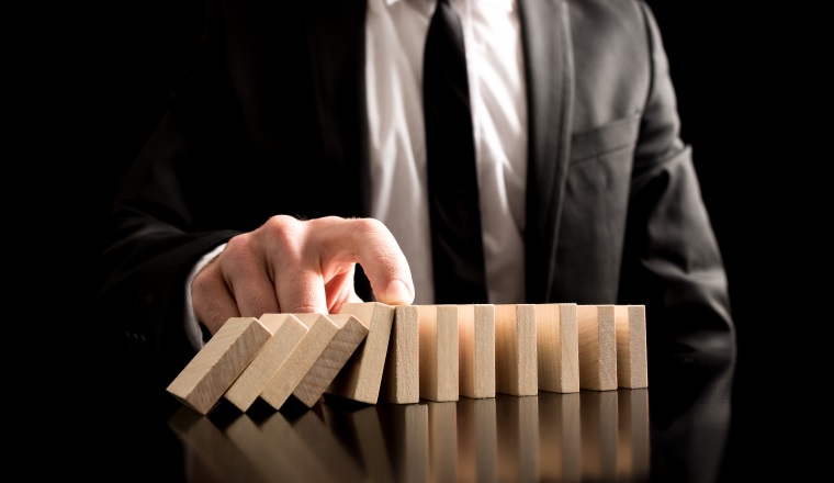 Businessman Stopping the Domino Effect from Small Wooden Blocks on the Table. A Creative Concept for Solution to Problem.