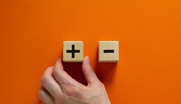Plus or minus. Businessman holds a cubes with plus icon. Wooden cube with minus icon. Beautiful orange background. Copy space. Business and plus and minus concept.