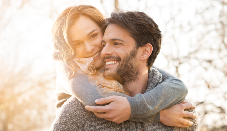 Closeup of smiling man carrying woman piggyback outdoor