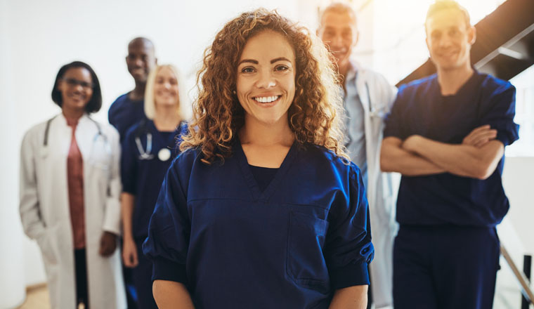 Smiling young female doctor standing in a hospital corridor with a diverse group of medical staff standing behind her