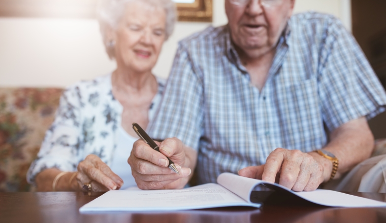 Senior couple signing will documents. Elderly caucasian man and woman sitting at home and signing some paperwork, focus on hands.