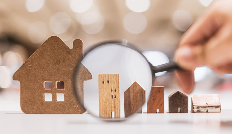 Hand holding magnifying glass and looking at house model, house selection, real estate concept.