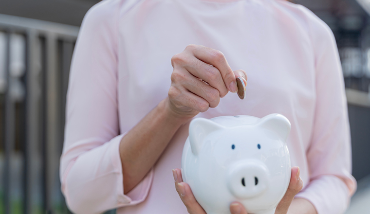 Happy Asian young woman putting a coin into a piggy saving box. Wealth, money saving for future investment concept. Coins stacked as a growth in financial for education wealth car and real estate.