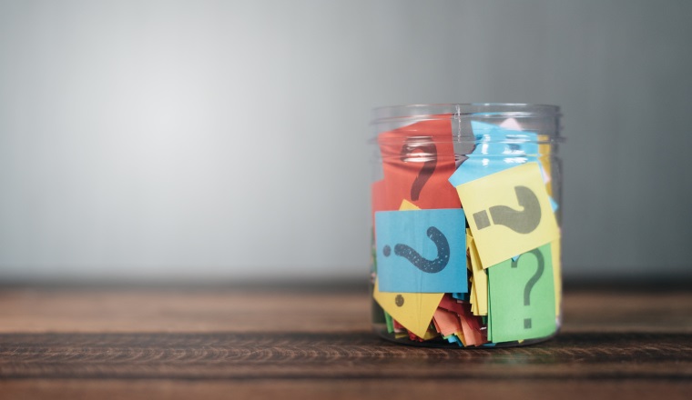 colorful paper with question mark in a plastic jar on wooden table. questions and diversity concept. FAQ and Q&A background concept