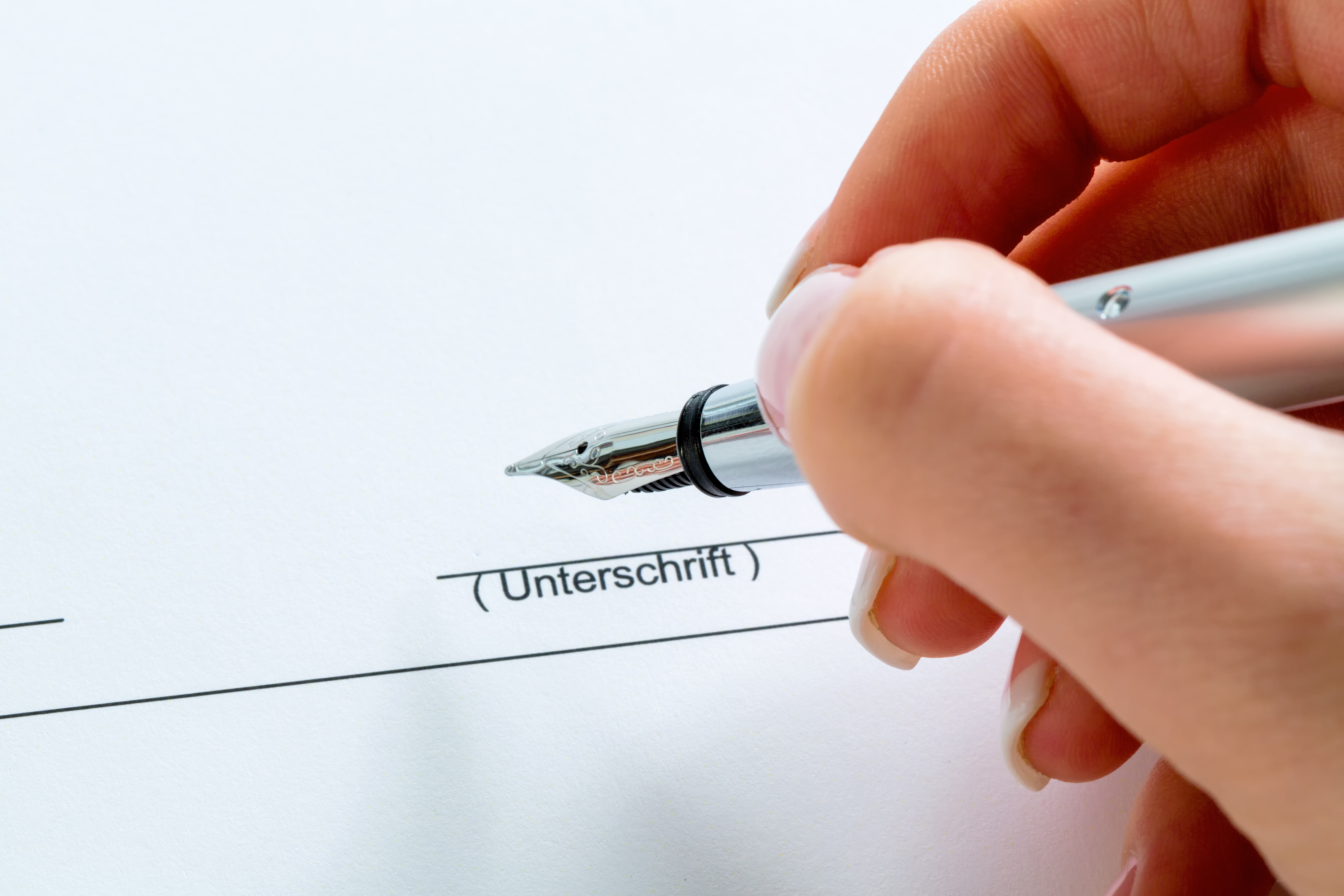 Eine Hand mit einer Füllfeder bei der Untrerschrift unter einem Vertrag oder Testament.