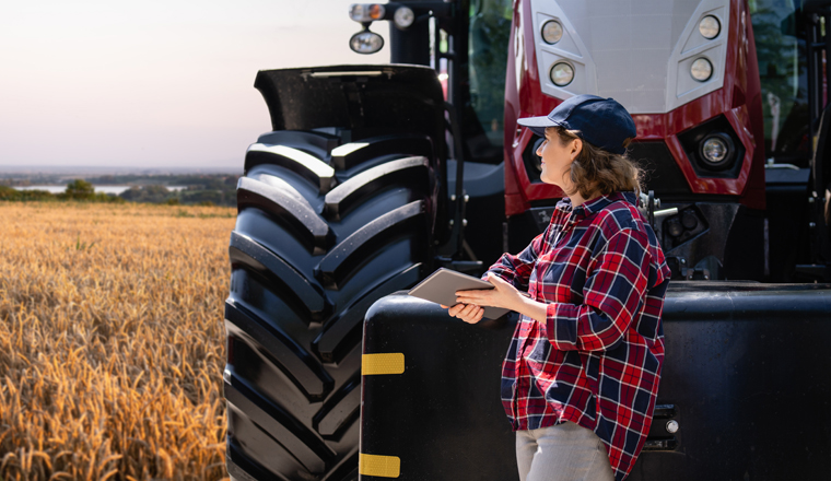 Female farmer with a digital tablet next to agricultural tractor.