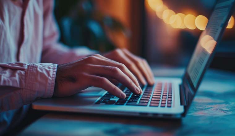 Close-up of a person's hands typing on a laptop keyboard