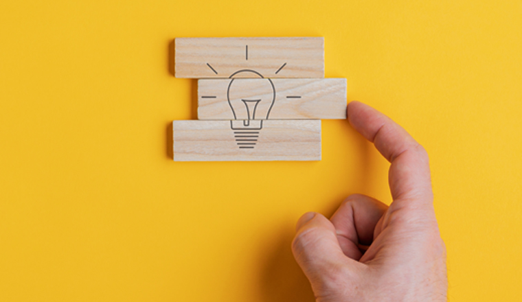 Wide view image of male hand assembling a light bulb drawing on wooden pegs in a conceptual image. Over yellow background.