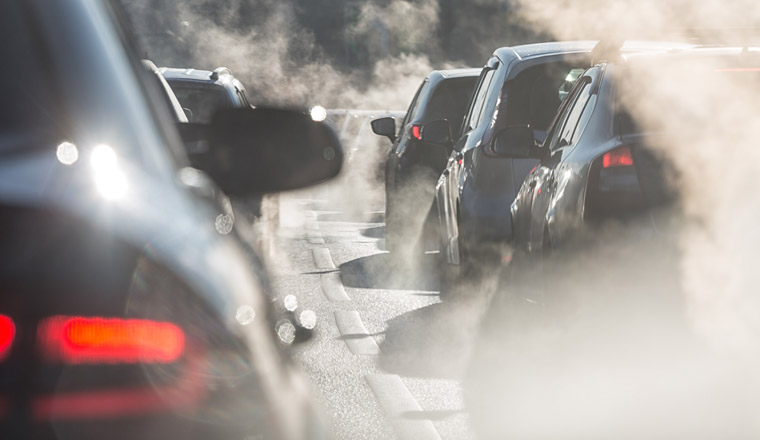 Blurred silhouettes of cars surrounded by steam from the exhaust pipes. Traffic jam 