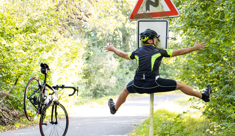 A falling cyclist bumps into a road sign warning about road with turns.