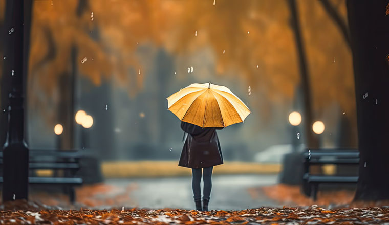 Young woman walking through a rainy park hiding under an umbrella as a man walks through wet slushy streets in a bad cloudy weather With copyspace for text