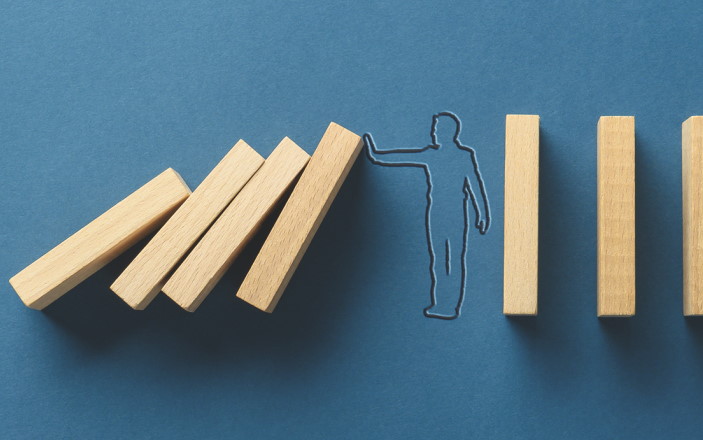 Silhouette of businessman on navy blue background stopping falling dominos in a conceptual image. With copy space.