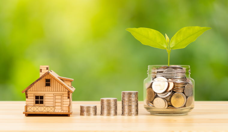 Coin jar and stack, and model house on wooden desk on green tree background, mortgage concept