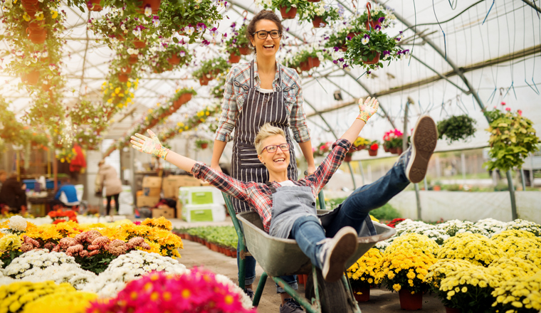 Two adorable joyful florist women having fun with cart for a break in the greenhouse.