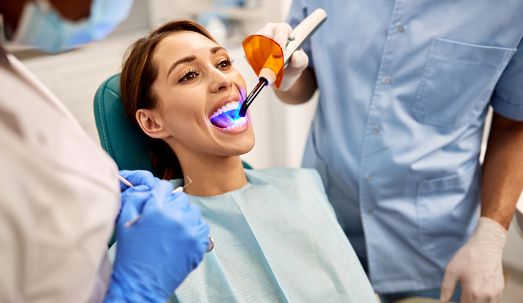 Young woman getting dental filling drying procedure with curing UV light at dental clinic.