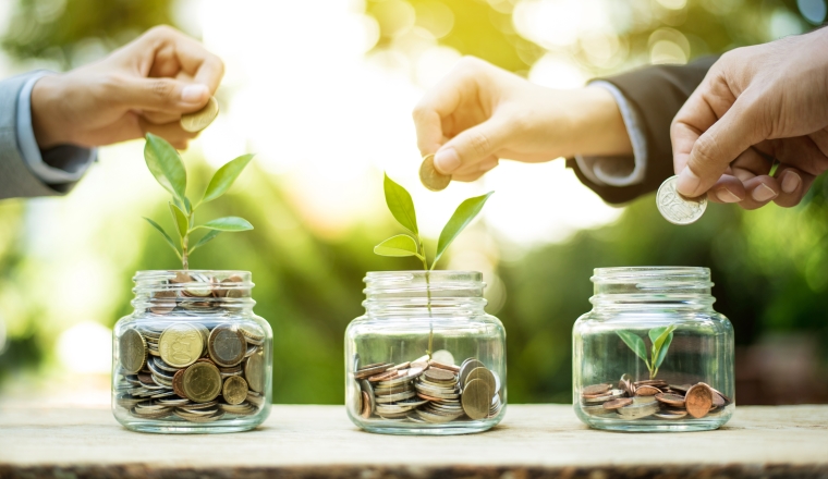 Businessman hands putting money (coin) into the glass jar - savings and investment  concept
