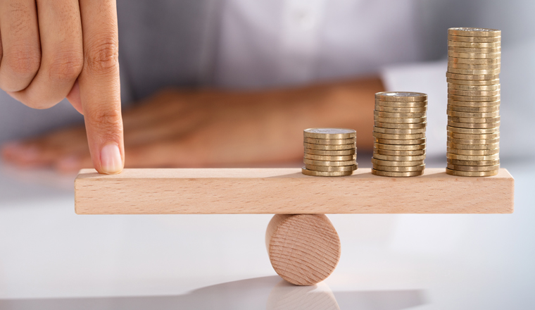 Close-up Of Businessperson's Finger Balancing Stacked Of Coins On Wooden Seesaw