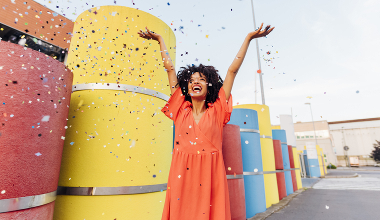 Playful woman throwing confetti by multi colored pipes