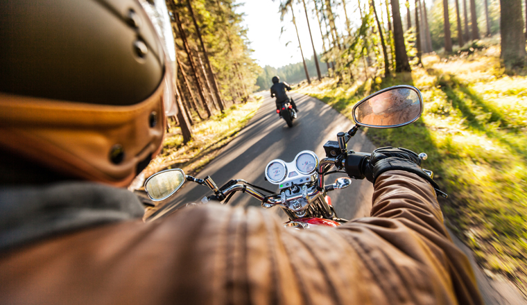 Man seat on the motorcycle on the forest road during sunrise.