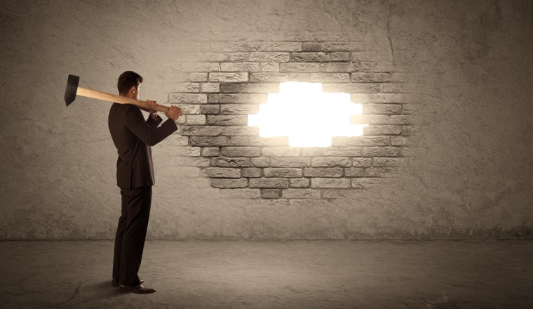 Business man hitting brick grungy wall with hammer and opening a hole