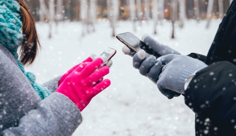 Couple using smartphone in winter with gloves for touch screens. Backgound