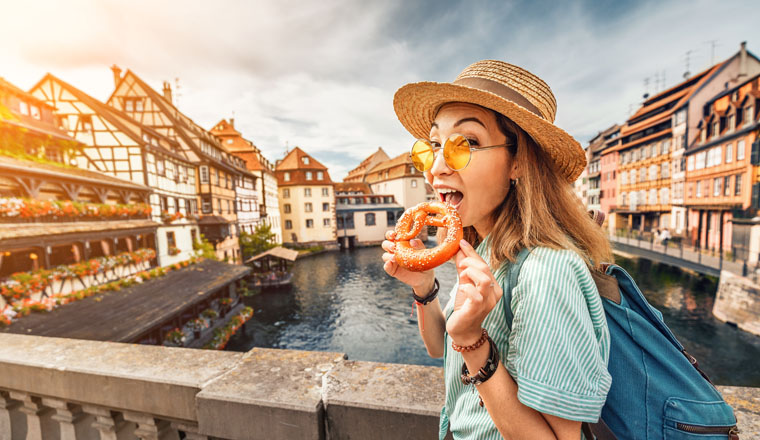 Happy asian girl tourist eating delicious pretzel while travelling in Europe. Tourism and food concept