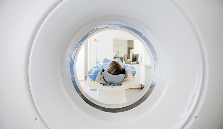 Young woman undergoing CT scan while doctor's using computers in hospital