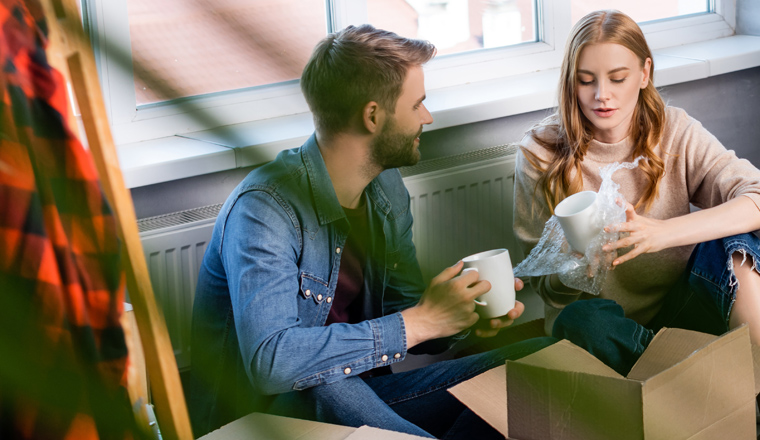 selective focus of joyful woman holding cup while unpacking box with boyfriend, panoramic shot