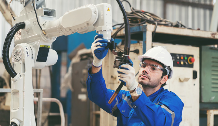 Male engineer worker repair automatic robotic arm in factory. Male technician worker inspecting quality automatic welding robot arm machine at production line