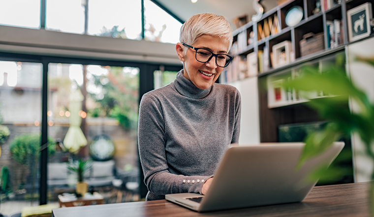 Portrait of a cheerful mature businesswoman working on laptop at home office.