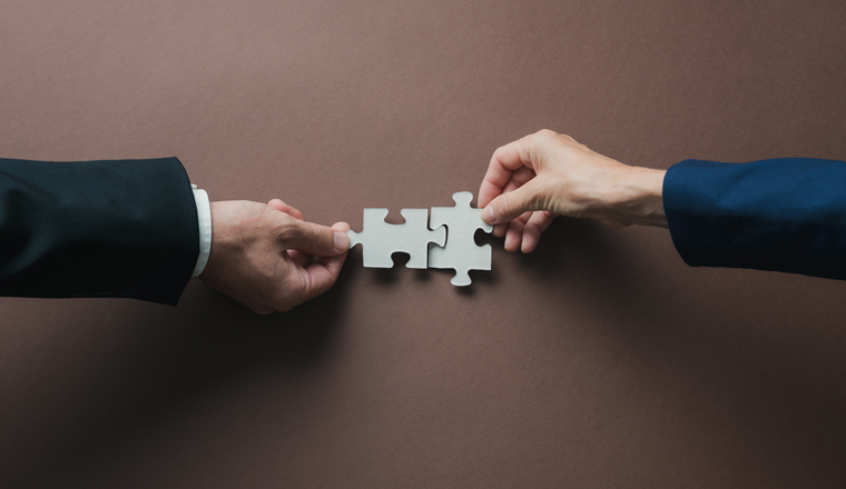 Teamwork and partnership conceptual image - hands of a businessman and businesswoman joining blank matching puzzle pieces over brown background.