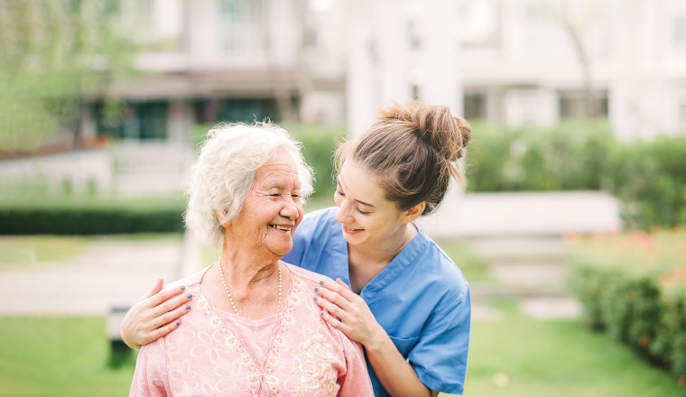 Smiling nurse caregiver with Asian elderly woman outdoor in the park