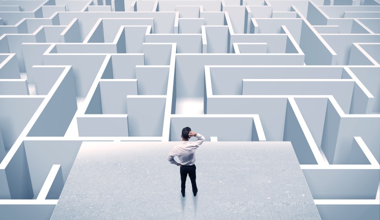 An elegant businessman standing on a square platform looking over infinite labyrinth concept