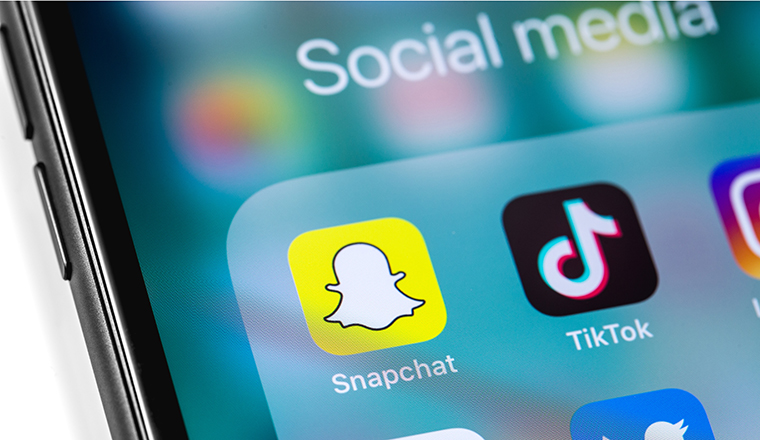 Social media apps. TikTok, Snapchat logo on the screen Apple iPhone with Earpods. Snapchat is a popular social media application for sharing messages, images and videos. Moscow, Russia - March 12, 2019