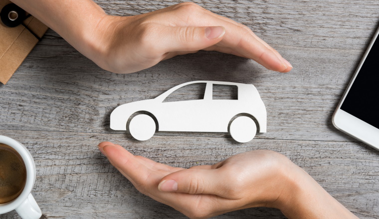 Hands protecting icon of car over wooden table. Top view of hands showing gesture of protecting car. Car insurance and automotive business concept.