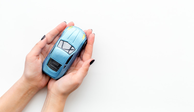 Car insurance concept. Safety of auto. Car toy in female hands on white background top view.