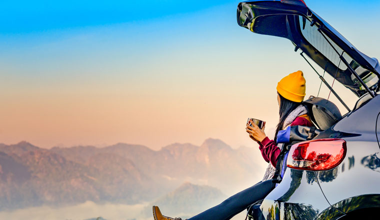 Woman traveller enjoy coffee time on back storage of car with scenery view of the mountain and mist morning in background