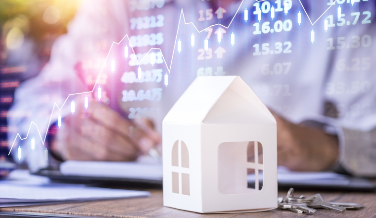 Businessman with model house and stock market chart background